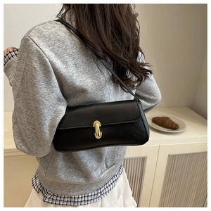 Detail of a black pebbled leather baguette bag featuring a gold oval clasp on model