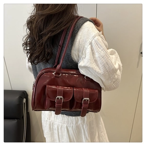Detail of dark red patent leather shoulder bag featuring dual pockets with silver buckles