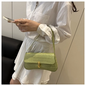 Green crocodile pattern baguette bag worn over the shoulder with a stylish white dress