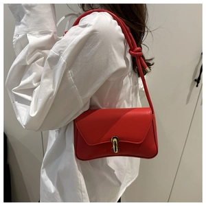 Détail du sac bandoulière en cuir rouge avec boucle dorée et bandoulière nouée élégante