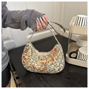 Detailed close-up of floral embroidery texture and gold metal plaque on crescent bag
