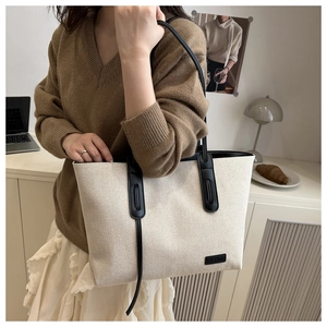 Dettaglio della borsa tote in tela con manici in pelle nera ed etichetta moda in scena