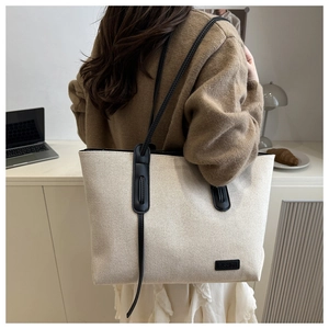 Vista posteriore di una modella con borsa tote in tela beige e profili neri alla moda