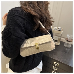 Close-up of a cream croc-embossed baguette bag with a gold buckle worn on the shoulder