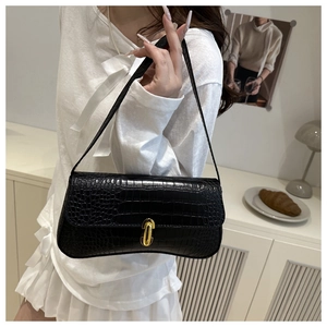 Gros plan du sac à bandoulière noir effet crocodile avec fermoir doré sur fond beige clair