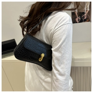 Close-up of black crocodile pattern shoulder bag with golden oval metal clasp on a model