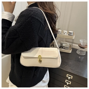 Close-up of cream-colored faux crocodile texture and gold oval buckle on underarm bag