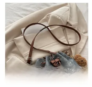 Detail of denim bucket bag with brown leather strap and plush bear charm on blazer