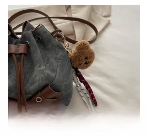 Detail of denim bucket bag showing side metal eyelets and brown plush bear charm