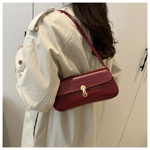 Detail of burgundy baguette bag featuring crocodile pattern and gold metal clasp
