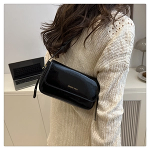 Close-up of black glossy patent leather shoulder bag with gold logo on a model