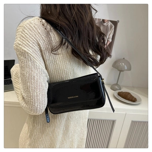 Model wearing black patent leather rectangular shoulder bag with vintage gold logo design