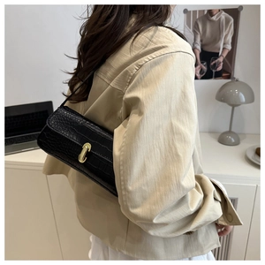 Detail of black crocodile pattern baguette bag with golden U-shaped buckle on shoulder