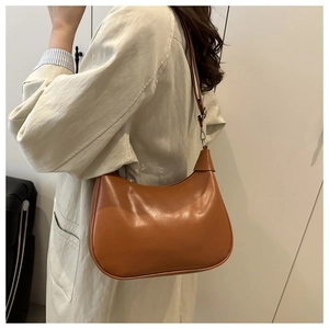 Side view of a caramel brown crescent shoulder bag worn by a model in a minimalist setting