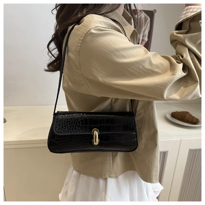 Detail of black crocodile texture underarm bag featuring an oval gold metal buckle
