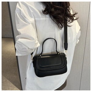 Detail of black crossbody bag featuring smooth faux leather and wide woven shoulder strap