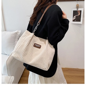 Detailed side view of white corduroy tote bag with chain strap and leather patch