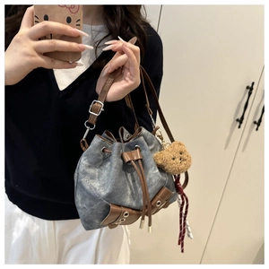 Close-up of vintage washed denim bucket bag with brown leather drawstrings and teddy bear charm