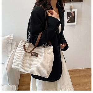 Detail of white corduroy tote bag featuring brown leather straps and silver metal chain link
