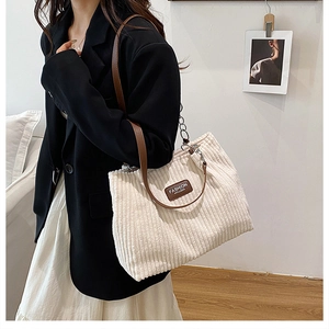 Detail of white corduroy tote bag featuring brown leather straps and silver metal chain