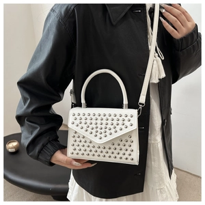 Detail of white structured crossbody bag featuring silver metal studs and curved handle