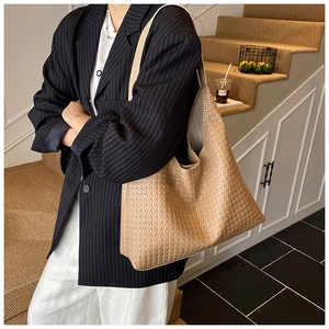 Close-up of a large khaki woven tote bag worn by a model in a stylish blazer