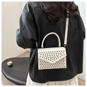 Detailed back view of a white studded crossbody bag worn by a model in a leather jacket
