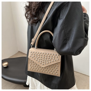 Close-up of beige rivet studded evening clutch bag with adjustable leather shoulder strap
