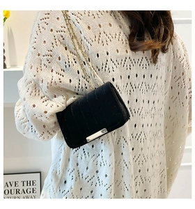 Close-up of a black quilted velvet chain bag with gold metal trim on a white sweater