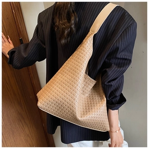 Side view of a woven leather tote bag in camel brown worn by a model in a striped suit
