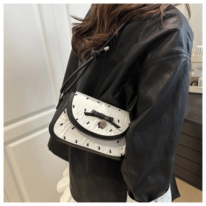 Detail der weißen Unterachseltasche mit Schleifendruck und Herzanhänger auf Lederjacke