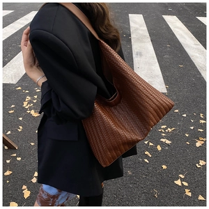 Detail of a large brown woven tote bag with crossbody strap for daily commute use