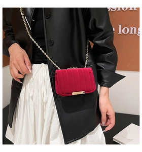 Detail of red velvet crossbody bag with vertical quilting and golden chain strap