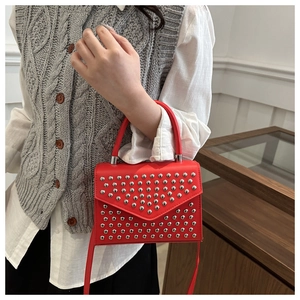 Detail of red crossbody bag with silver rivet studs and a top handle on a stylish model