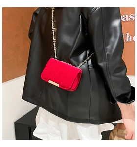 Detail of red suede mini square bag featuring a gold chain strap and metal trim on model