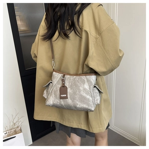 Détail du sac bandoulière industriel argenté avec lanières brunes sur un manteau kaki