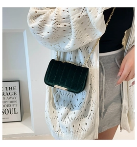 Detail of dark green velvet crossbody bag featuring golden chain and metal base accent