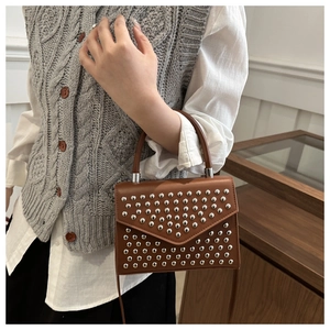 Detail view of brown leather crossbody bag featuring silver rivets and envelope flap design
