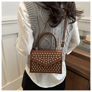 Brown leather crossbody bag with silver stud rivets worn over a grey knit vest
