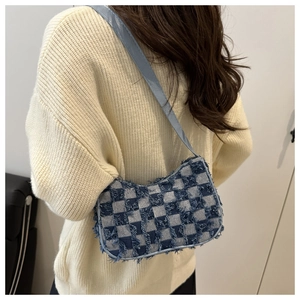 Blue checkerboard canvas shoulder bag with frayed edge texture on a knit sweater