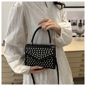 Detailed view of black rivet shoulder bag held by model wearing a white dress