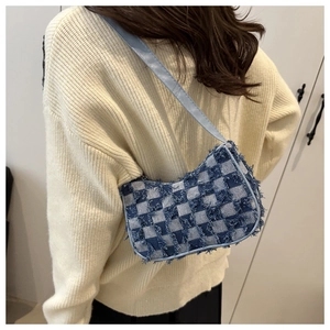 Detail of blue checkerboard denim baguette bag with frayed edges worn by a model