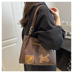 Side view of a large brown canvas tote bag with letter print and dog patch detail