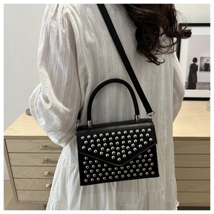Detail of a black leather crossbody bag featuring silver stud accents on a white dress