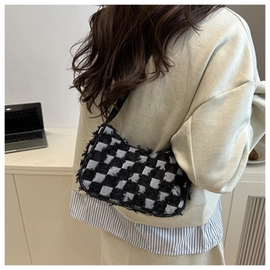 Detailed view of black and white checkerboard tweed baguette bag on person shoulder