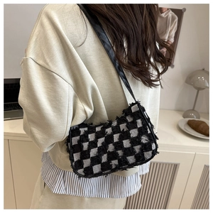 Detail of checkered baguette bag with fringe texture and black leather strap worn by model