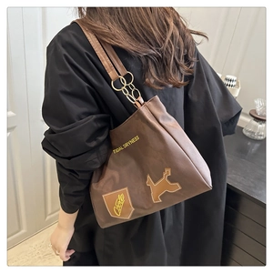 Dettaglio di una borsa tote marrone con anelli dorati sulla tracolla e stampa testuale