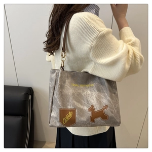 Dettaglio borsa shopper grigia con scritta Tidal Dryness, manici marroni e patch cane