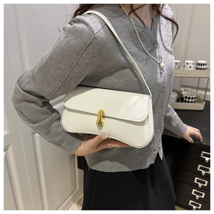 Detail shot of a cream-colored baguette bag with golden twist lock and lychee leather texture