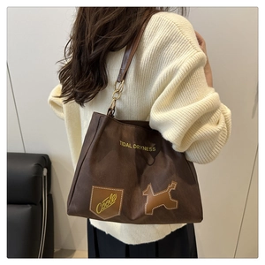 Detail of dark brown suede tote bag with chain strap and cute dog patch on a model